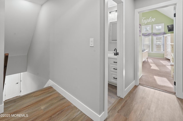 hall with light hardwood / wood-style flooring, vaulted ceiling, and sink