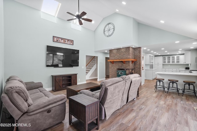 living room with a fireplace, light hardwood / wood-style floors, high vaulted ceiling, and ceiling fan