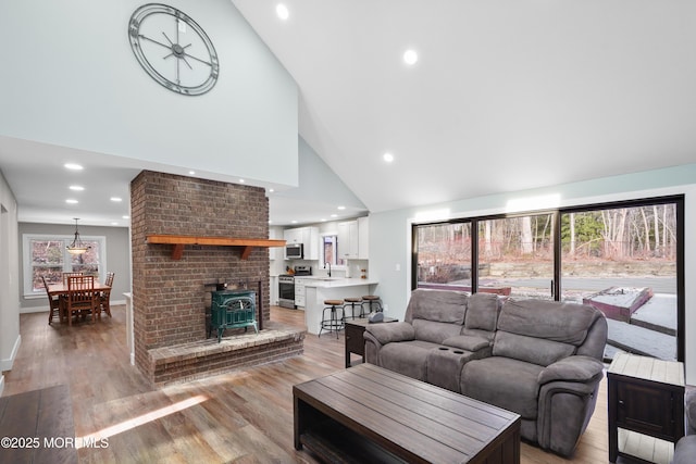 living room featuring a wood stove, sink, high vaulted ceiling, and light hardwood / wood-style flooring