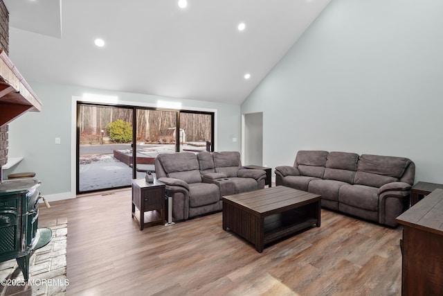 living room with a wood stove, light hardwood / wood-style flooring, and high vaulted ceiling