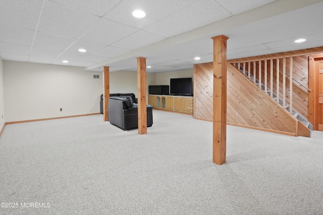 basement featuring carpet flooring, a drop ceiling, and wooden walls