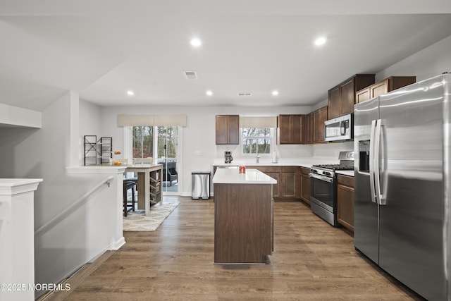 kitchen with dark brown cabinets, a center island, light wood-type flooring, and appliances with stainless steel finishes