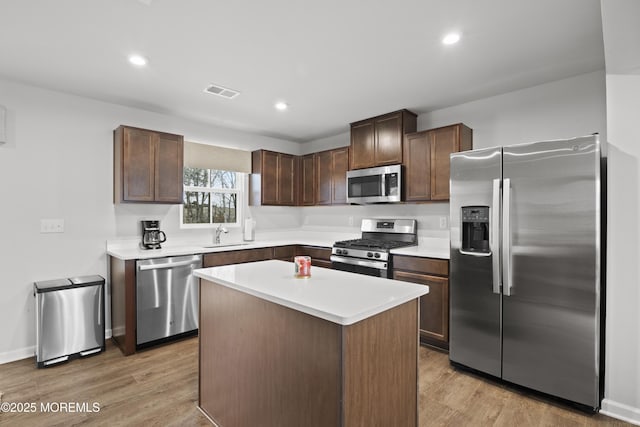 kitchen featuring light wood-type flooring, stainless steel appliances, a kitchen island, and dark brown cabinetry