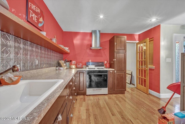 kitchen featuring light wood-type flooring, gas range gas stove, wall chimney range hood, and sink