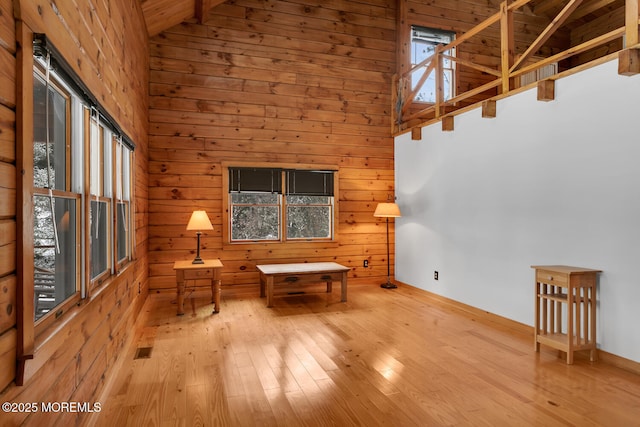 unfurnished room featuring wooden walls, high vaulted ceiling, and light hardwood / wood-style floors