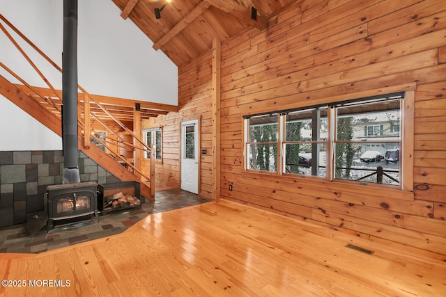 unfurnished living room featuring a wood stove, high vaulted ceiling, beamed ceiling, wood-type flooring, and wood ceiling