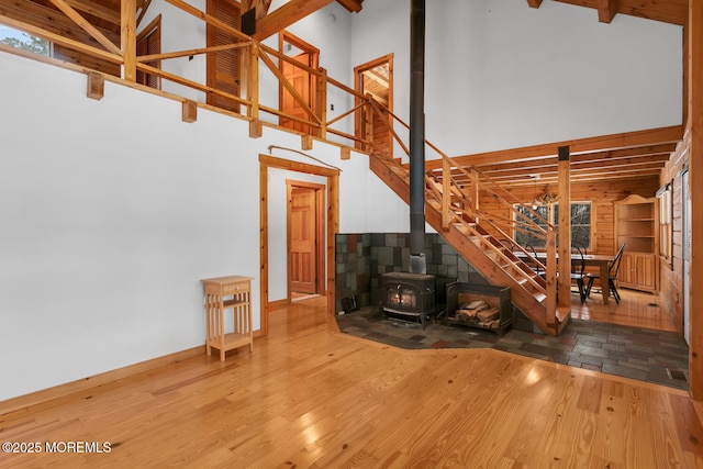 stairs featuring beam ceiling, a wood stove, a towering ceiling, and wood-type flooring