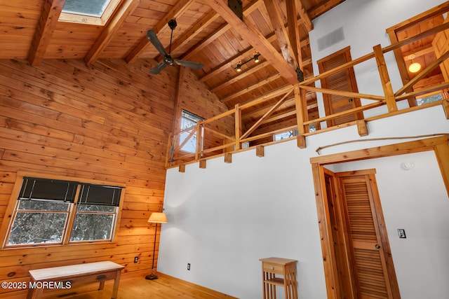 living room featuring a skylight, ceiling fan, beamed ceiling, wood walls, and wood ceiling