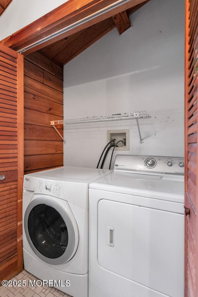 clothes washing area featuring washing machine and dryer, wood walls, and light tile patterned floors