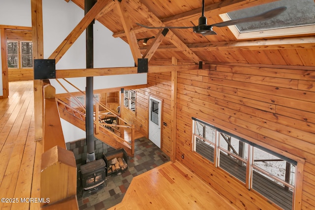 unfurnished living room with hardwood / wood-style floors, wood walls, wooden ceiling, lofted ceiling with skylight, and ceiling fan