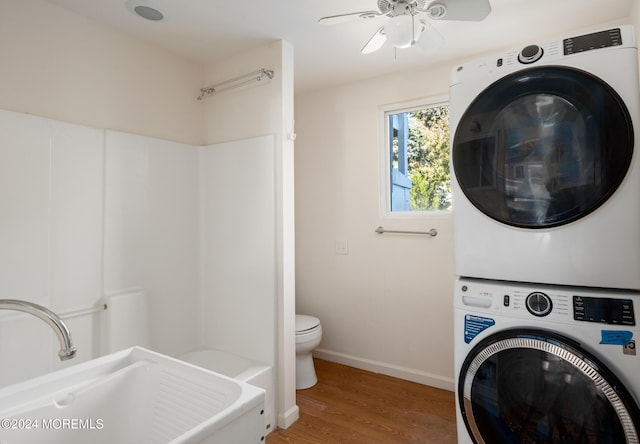 clothes washing area with hardwood / wood-style flooring, ceiling fan, stacked washing maching and dryer, and sink