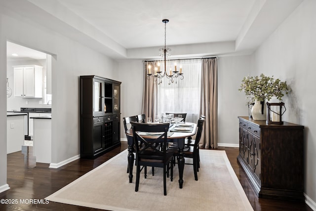 dining area with a chandelier, a tray ceiling, dark wood-style flooring, and baseboards