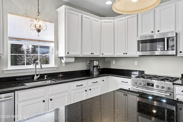 kitchen with appliances with stainless steel finishes, sink, dark stone countertops, white cabinetry, and hanging light fixtures