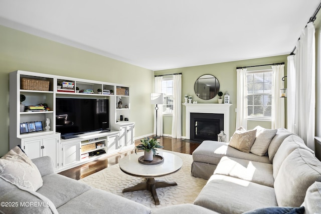 living area featuring a fireplace with flush hearth, baseboards, and wood finished floors