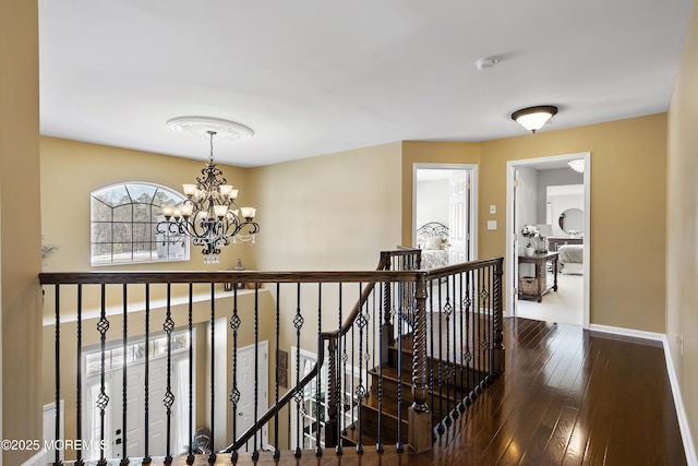 hall with wood-type flooring, baseboards, a notable chandelier, and an upstairs landing