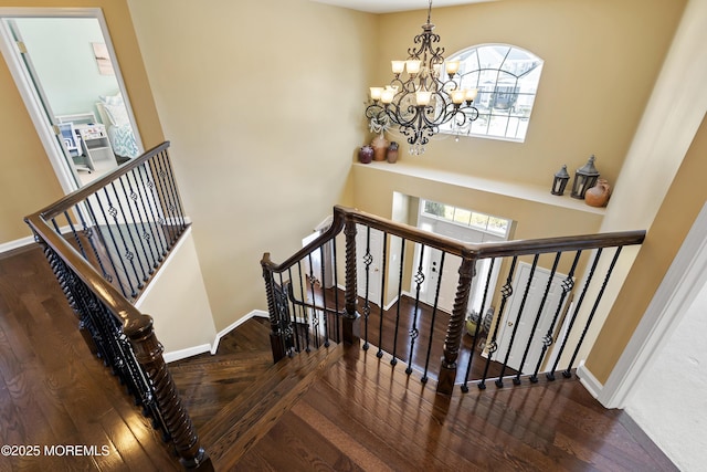 stairs featuring wood finished floors, baseboards, and an inviting chandelier