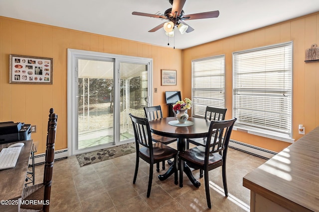 tiled dining area featuring ceiling fan, baseboard heating, a wealth of natural light, and wooden walls