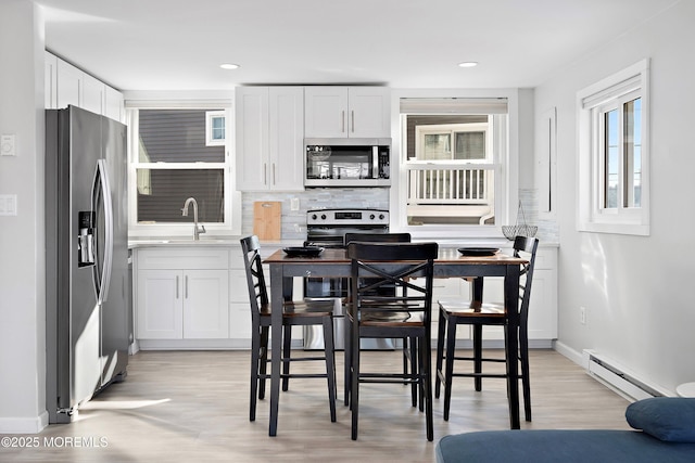 kitchen featuring stainless steel appliances, white cabinets, baseboard heating, and tasteful backsplash