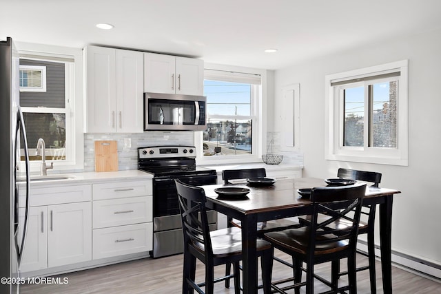 kitchen with light hardwood / wood-style floors, a baseboard heating unit, white cabinetry, appliances with stainless steel finishes, and sink