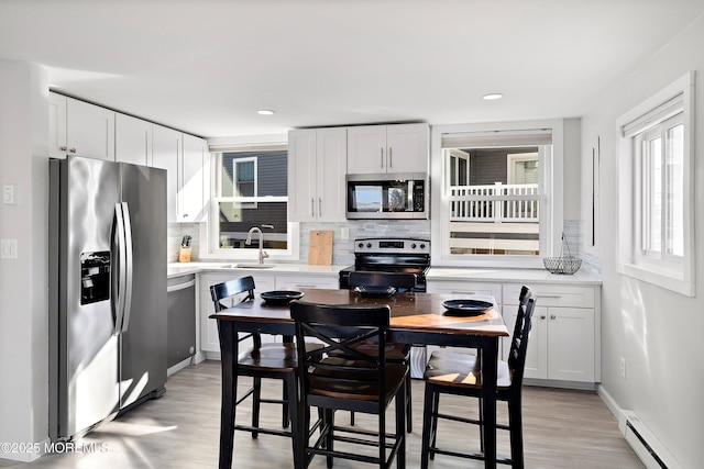 kitchen featuring stainless steel appliances, decorative backsplash, white cabinets, a baseboard radiator, and sink