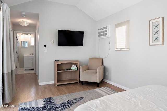 bedroom with lofted ceiling, ensuite bath, an AC wall unit, and wood-type flooring