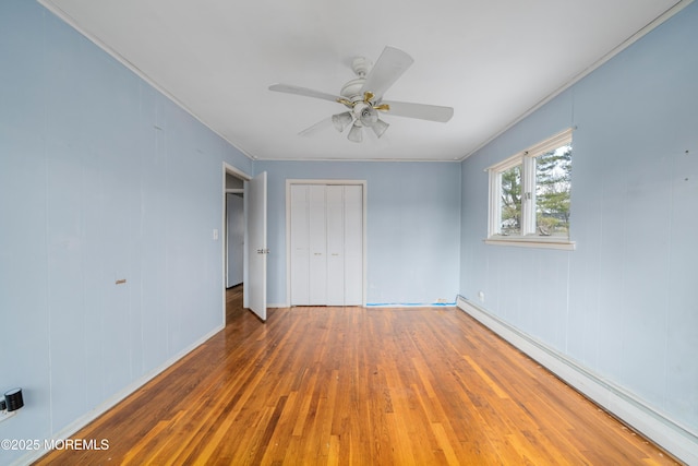 unfurnished bedroom with ceiling fan, a closet, dark wood-type flooring, and a baseboard heating unit