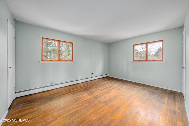 empty room featuring baseboard heating, a healthy amount of sunlight, and wood-type flooring