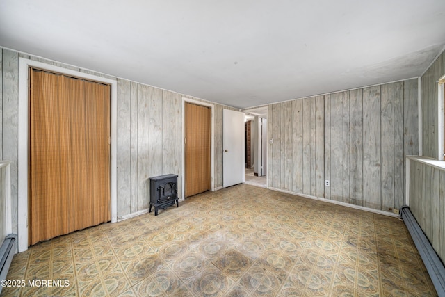 interior space featuring a closet, a wood stove, baseboard heating, and wood walls