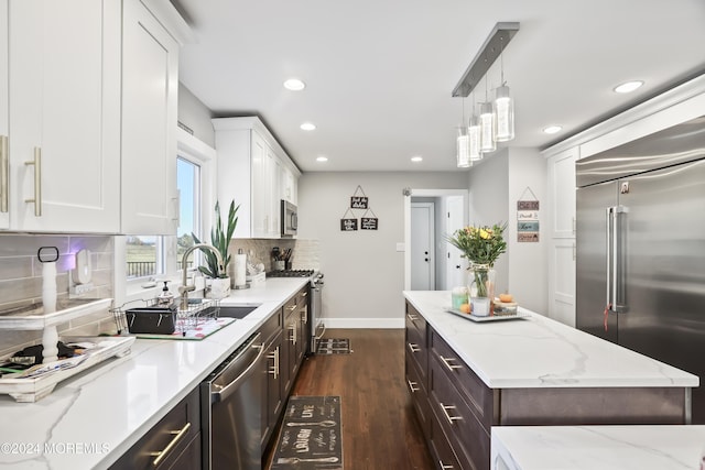 kitchen with sink, light stone countertops, appliances with stainless steel finishes, decorative light fixtures, and white cabinetry