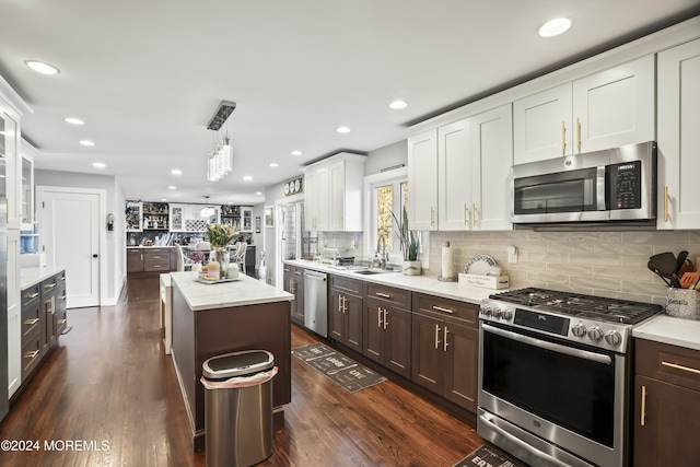 kitchen featuring stainless steel appliances, a kitchen island, dark wood-type flooring, white cabinetry, and hanging light fixtures