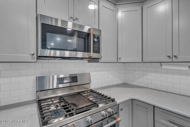 kitchen with light stone countertops, appliances with stainless steel finishes, gray cabinetry, and tasteful backsplash