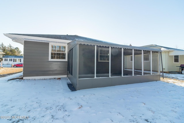 snow covered rear of property with a sunroom