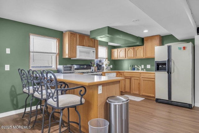 kitchen with white appliances, ventilation hood, kitchen peninsula, light wood-type flooring, and a breakfast bar