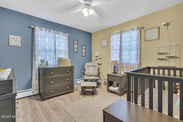 bedroom featuring ceiling fan, a baseboard heating unit, a nursery area, and light wood-type flooring