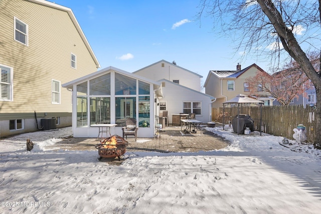 snow covered rear of property featuring cooling unit, an outdoor fire pit, and a sunroom