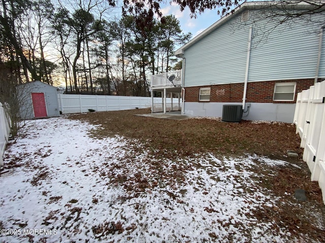 yard covered in snow featuring a storage unit, a balcony, and central AC