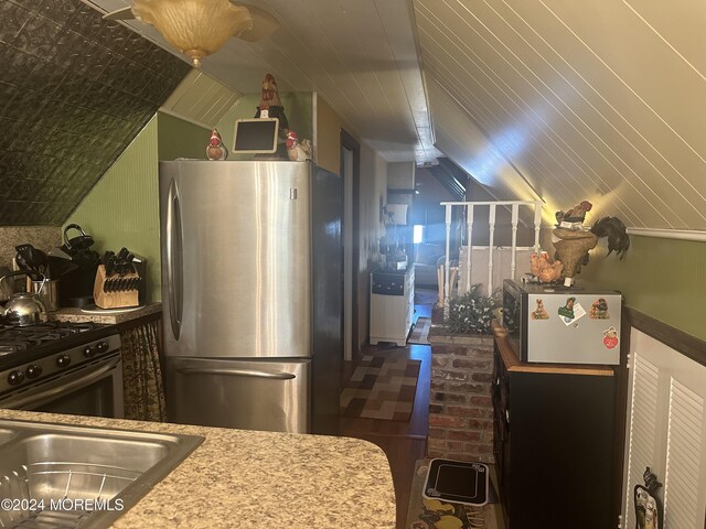 kitchen featuring gas range oven, stainless steel fridge, and vaulted ceiling