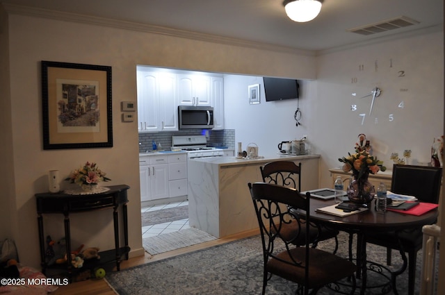 kitchen featuring light hardwood / wood-style flooring, a breakfast bar area, decorative backsplash, white cabinets, and ornamental molding