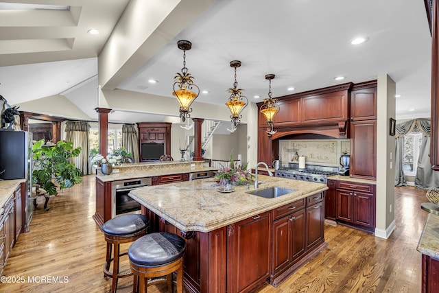 kitchen with sink, an island with sink, hanging light fixtures, and appliances with stainless steel finishes