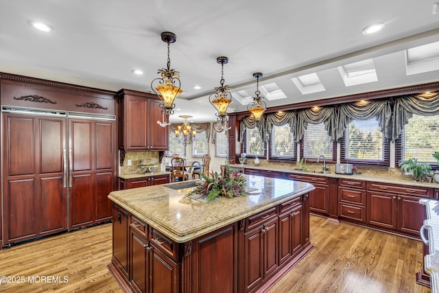 kitchen with light stone countertops, pendant lighting, light hardwood / wood-style flooring, a notable chandelier, and a kitchen island