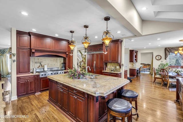 kitchen featuring hanging light fixtures, paneled built in refrigerator, an island with sink, tasteful backsplash, and a kitchen bar