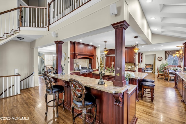 kitchen with ornate columns, a high ceiling, light hardwood / wood-style floors, hanging light fixtures, and a breakfast bar area