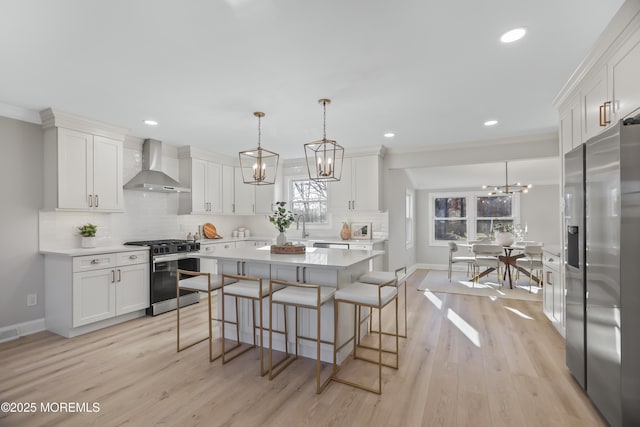 kitchen with appliances with stainless steel finishes, white cabinets, hanging light fixtures, and wall chimney exhaust hood