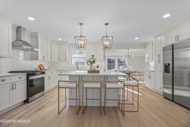 kitchen with light hardwood / wood-style flooring, hanging light fixtures, stainless steel appliances, wall chimney range hood, and white cabinets