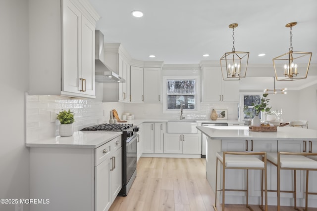 kitchen with stainless steel gas range, pendant lighting, wall chimney exhaust hood, white cabinets, and sink