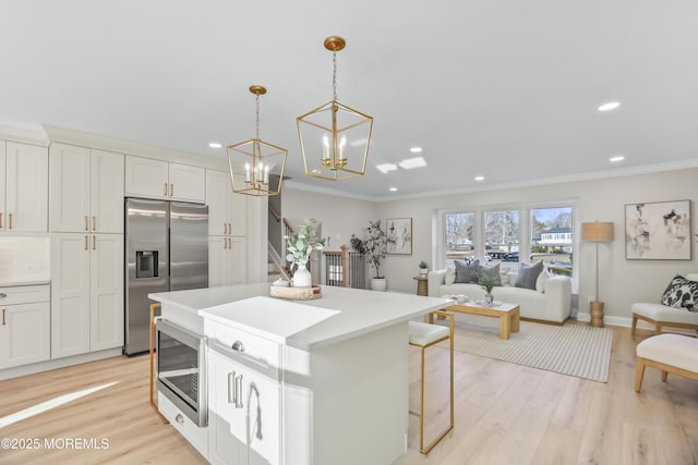 kitchen with appliances with stainless steel finishes, light hardwood / wood-style floors, a center island, white cabinetry, and decorative light fixtures