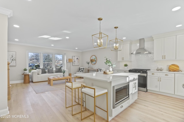 kitchen featuring white cabinetry, stainless steel stove, a center island, wall chimney range hood, and built in microwave