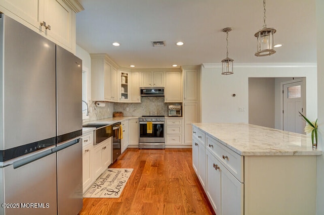 kitchen featuring light stone countertops, stainless steel appliances, backsplash, decorative light fixtures, and exhaust hood