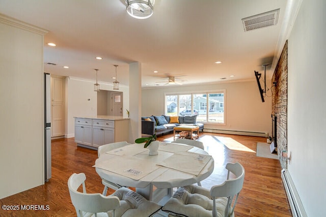 dining area featuring a fireplace, hardwood / wood-style flooring, crown molding, and a baseboard heating unit