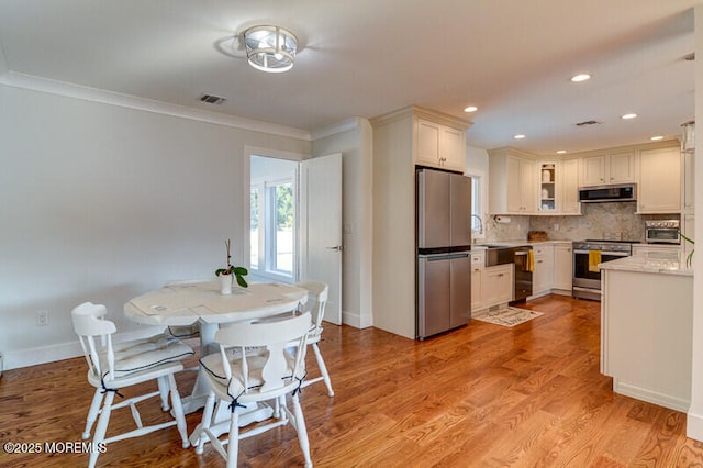 kitchen with white cabinetry, stainless steel appliances, tasteful backsplash, exhaust hood, and light wood-type flooring